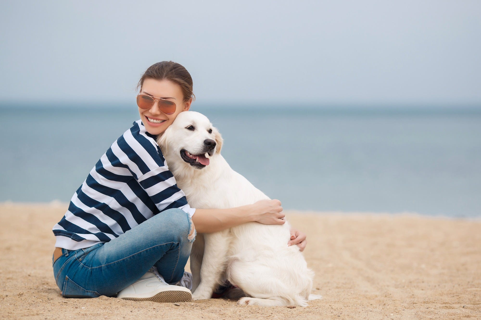 Woman on beach hugging labrador retriever